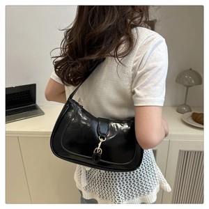 Detail shot of a black glossy leather hobo bag with gold piston clasp on a person