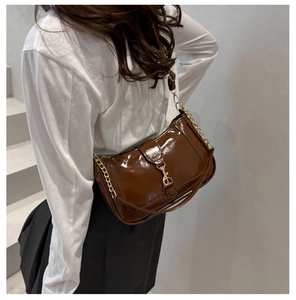 Detail of a brown patent leather shoulder bag with gold chain strap and metal buckle