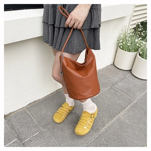 Brown litchi grain leather bucket bag with metallic chain detail held by a model