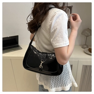 Close-up of black patent leather crescent hobo bag with a gold buckle worn on shoulder