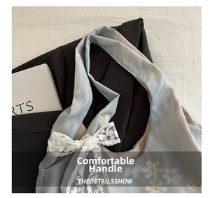 Detail of light blue handbag with white flower embroidery and lace bow on handle