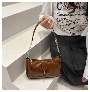 Detail of a brown patent leather underarm bag with glossy finish and gold metal chain strap