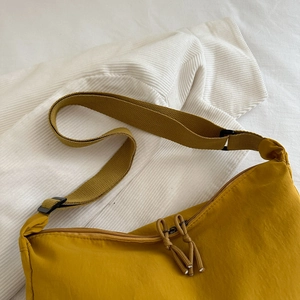 Minimalist ginger yellow nylon crossbody bag with adjustable strap on white textured surface