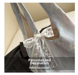 Detail of light blue fabric featuring white lace bow and delicate floral embroidery