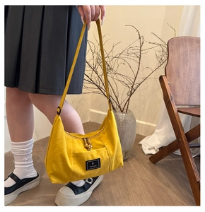 Detail of yellow canvas crossbody bag with front pocket and branded logo tag