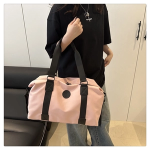 Detail of pink travel tote featuring wide black straps and circular logo on large canvas bag