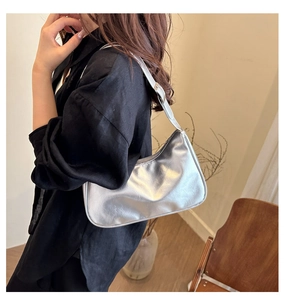 Silver crescent underarm bag with metallic patent finish shown on model shoulder