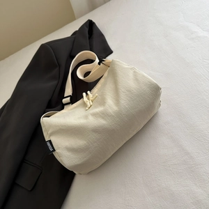 Minimalist cream nylon crossbody bag with black brand label and wide shoulder strap