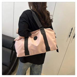 Model carrying a pink large capacity travel duffel bag with black straps in a modern room