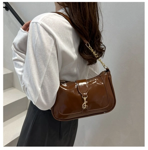 Detail of dark brown patent leather shoulder bag with golden piston buckle on model