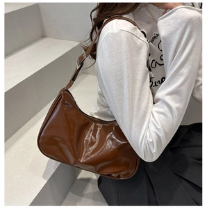 Close-up of brown glossy minimalist shoulder bag with vintage crinkle texture and silver buckle