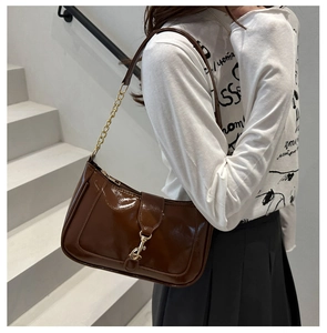 Detail of glossy brown shoulder bag featuring gold metal buckle and leather chain strap