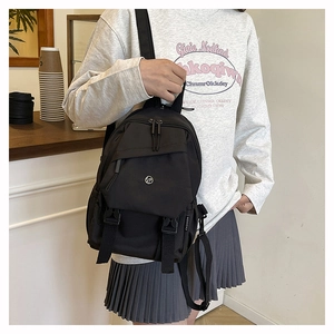 Detail of a black nylon backpack featuring adjustable buckle straps and a fashion label