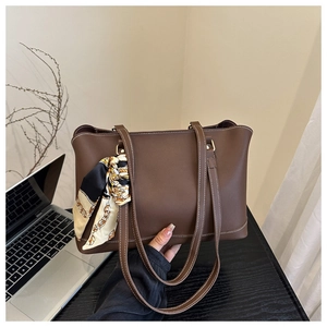 Detail of brown leather tote bag with white contrast stitching and decorative floral scarf