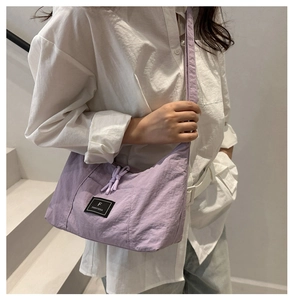 Detail of lavender nylon crossbody bag with black brand label and soft knot strap detail