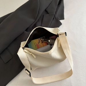 Waterproof off-white nylon crossbody bag with wide strap on a minimal background