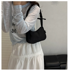 Detail of minimalist black nylon underarm bag with stylish ruffled shoulder strap design