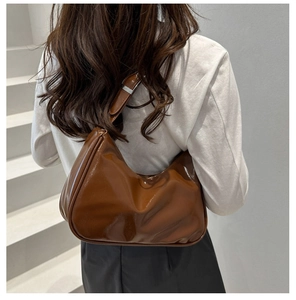 Close-up of a brown glossy leather hobo bag with adjustable strap and silver buckle