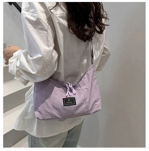Close-up of lavender nylon tote bag featuring adjustable black strap and brand tag