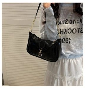 Detail of black glossy underarm bag with gold chain strap and metal clasp on model