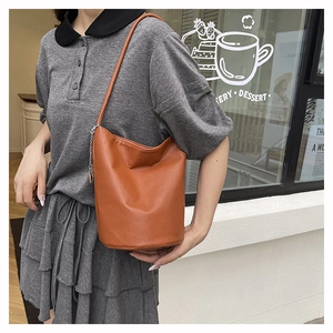 Close-up of caramel litchi grain leather bucket bag with slim strap and metal chain detail