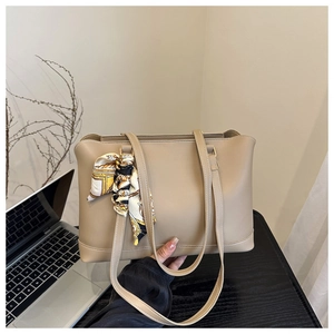 Close-up of khaki tote bag with a decorative floral scarf on the handle next to a laptop