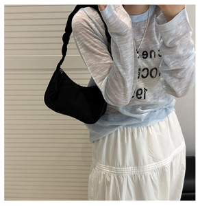 Detail of a black nylon crescent shoulder bag paired with a blue long-sleeve graphic tee