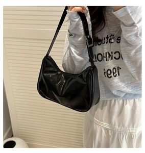 Minimalist black patent leather hobo bag worn by a model in a casual outfit