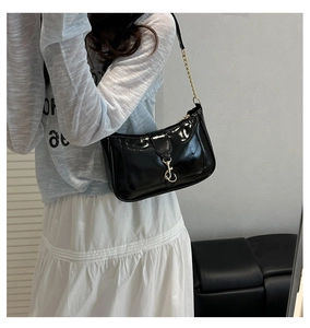 Detail of black patent leather shoulder bag with gold chain and metal hook closure