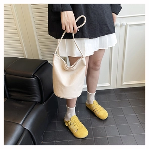 Detail of a creamy white leather bucket bag paired with stylish yellow hollow-out sandals