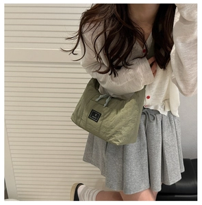 Detail of green nylon crossbody bag with dual zipper closure and logo patch