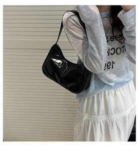 Detail of a black patent leather underarm hobo bag on a model with a glossy finish
