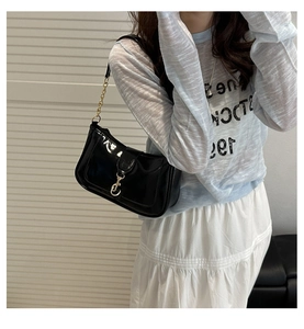 Close-up of black patent leather underarm bag with gold horsebit buckle and chain strap