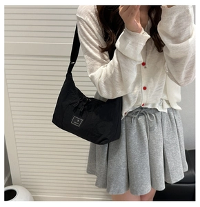 Detail of adjustable strap and square logo patch on black nylon crossbody dumpling bag