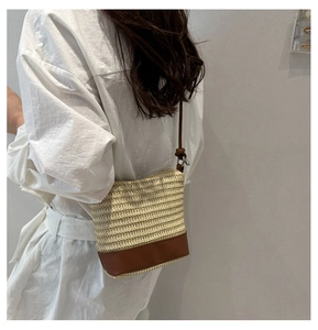 Detail of hand-woven straw crossbody bag with brown leather strap worn by a model