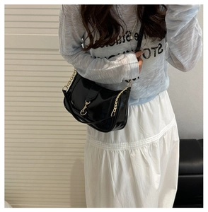 Detail of black patent leather shoulder bag with metallic chain and hook closure