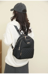 Close-up of black quilted nylon backpack with gold zippers worn by a model