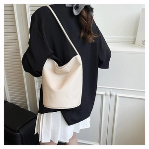 Detail of off-white bucket bag featuring lychee grain texture and minimalist shoulder strap