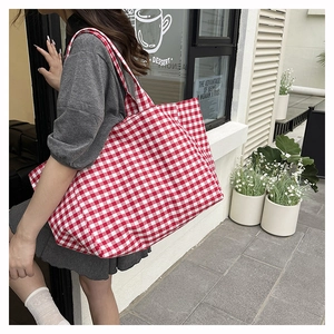 Détail d'un sac cabas en toile à carreaux vichy rouge et blanc porté par un mannequin