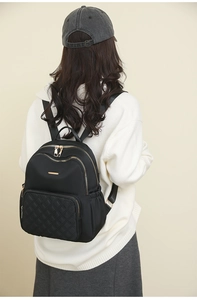 Close-up of black quilted nylon backpack featuring gold zippers on a female model
