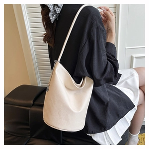 Minimalist beige bucket bag with litchi grain leather texture on a shoulder strap