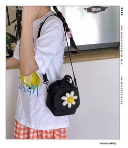 Close-up of black canvas crossbody bag with white flower charm worn by a model
