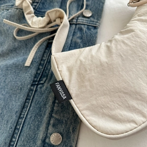 Minimalist creamy white nylon crescent underarm bag on blue denim jacket background