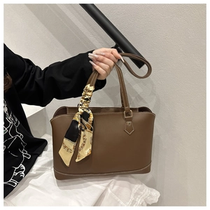 Close-up of brown leather tote bag with silk scarf accessory and detailed white stitching