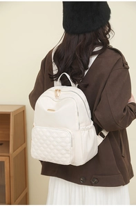 Rear view of a model wearing a quilted white nylon backpack with elegant gold zippers