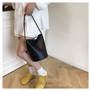 Detail of a black leather bucket bag featuring a slender strap and silver chain charm