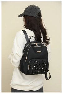 Rear view of a black nylon backpack with gold studs and quilted pockets on a model