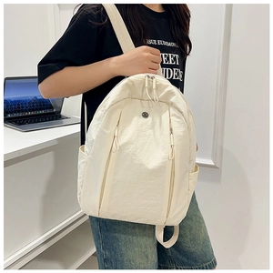 Detail view of cream nylon backpack featuring dual front zipper pockets and side pouch