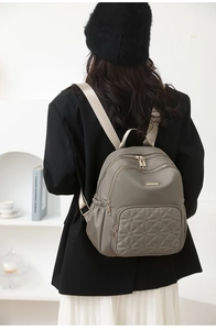 Detail view of taupe nylon backpack with geometric quilting and metallic zippers on back