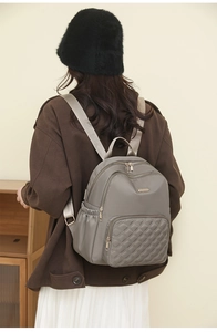 Detail showing the quilted diamond pattern and golden zipper on the grey nylon backpack